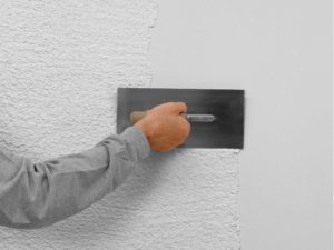 Arm von Handwerker verarbeitet weißen Stolit-Putz mit Kelle an der Wand 