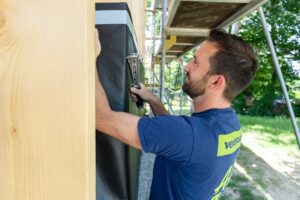 Handwerker bringt Winddichtigkeitsfolie an Holzkonstruktion einer VHF Hausfassade an.