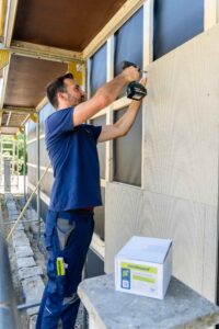 Handwerker mit Akku-Schrauber an der Fassade: Die VeroBoard AllStar Putzträgerplatten werden im Versatz direkt auf die Traglattung geschraubt und stumpf gestoßen.