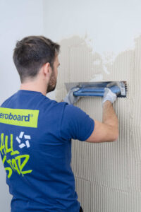 Handwerker trägt VeroBoard AllStar Kombi-Mörtel mit Zahntraufel auf Wand auf.