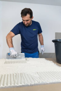 Handwerker trägt VeroBoard AllStar Kombi-Mörtel mit Zahntraufel auf der Platte auf.