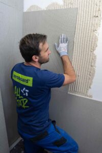 Handwerker presst VeroBoard AllStar Anti-Schimmelplatte in Mörtelschicht der Innenwand ein.