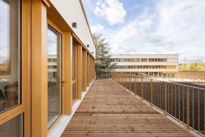 Außenaufnahme Obergeschoss mit Balkon an Fensterreihe: Die neue Schule „Collège Claudine Hermann in Massy, südlich von Paris, ist ein Neubau mit hohem Anspruch: Mit einem U-Wert von 0,15 W/m²K sind die Wände hochdämmend, zugleich zeigt sich der Neubau auch besonders attraktiv gestaltet. Die helle, fugenlose Putzfassade ist auch an den gerundeten Innen- und Außenecken von höchster handwerklicher Qualität.
