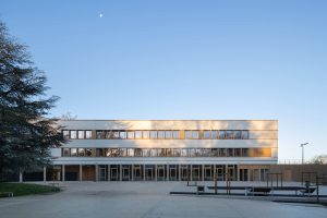 Außenaufnahme vom Schulgebäude und Schulhof: Die neue Schule „Collège Claudine Hermann in Massy, südlich von Paris, ist ein Neubau mit hohem Anspruch: Mit einem U-Wert von 0,15 W/m²K sind die Wände hochdämmend, zugleich zeigt sich der Neubau auch besonders attraktiv gestaltet. Die helle, fugenlose Putzfassade ist auch an den gerundeten Innen- und Außenecken von höchster handwerklicher Qualität.