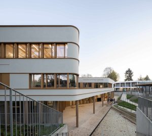 Außenaufnahme vom Eingangsbereich: Die neue Schule „Collège Claudine Hermann in Massy, südlich von Paris, ist ein Neubau mit hohem Anspruch: Mit einem U-Wert von 0,15 W/m²K sind die Wände hochdämmend, zugleich zeigt sich der Neubau auch besonders attraktiv gestaltet. Die helle, fugenlose Putzfassade ist auch an den gerundeten Innen- und Außenecken von höchster handwerklicher Qualität.