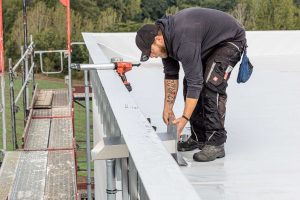 Handwerker beim nächsten Bauschritt auf dem Flachdach: Dann wird der Speier einfach durch die Öffnung gesteckt.