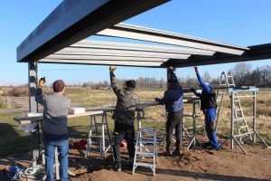 Vier Männer beim manuellen Einbau von Glasscheiben an einer Überdachung. - Auf Theorie folgt Praxis: Im Seminar „Montage“ legen die Teilnehmenden Hand an.