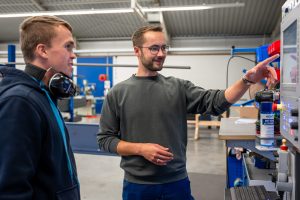 In der Werkshalle von TS Aluminium: Zwei Männer bei der Einweisung an der technsichen Anlage. - Der Workshop „Dachzuschnitt“ findet direkt „an der Säge“ in der Fertigung statt.