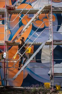 TEA KVAR schafft an der Fassade des Studierendenwohnheims im Jungbusch (Mannheim) das farbenfrohe Wandbild „Forever Jungbusch“. Für die kräftigen Orange- und Blautöne setzt die kroatische Künstlerin auf die Fassadenfarbe StoColor Dryonic vom Projektpartner Sto. Die langlebigen und farbintensiven Beschichtungssysteme tragen dazu bei, dass die großflächigen Kunstwerke dauerhaft ihre Strahlkraft entfalten können.