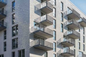 Außenaufnahme der Fassadenecke mit Klinker und Balkonen des Sportlerhaus in HafenCity Hamburg. Die hellgrauen Keramikmodule der Fassade bilden eine robuste und gestalterisch anspruchsvolle Oberfläche. Je nach Blickwinkel und Tageszeit ändert sich die Ansicht der teils dreidimensionalen Fläche.