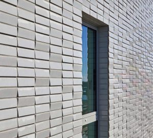Außenaufnahme von Fassade um ein Fenster des Sportlerhaus in HafenCity Hamburg. Die Fassade erzeugt durch die Neigungswechsel eine subtile Reflexion des Lichts ohne erkennbares Muster.