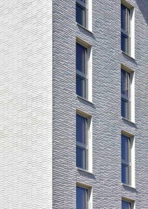 Außenaufnahme von Ecke der Fassade des Sportlerhaus in HafenCity Hamburg. Die Fassade erzeugt durch die Neigungswechsel eine subtile Reflexion des Lichts ohne erkennbares Muster.