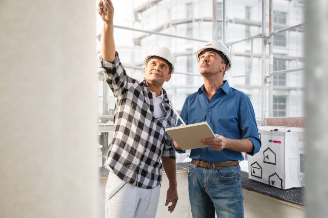 Zwei Männer auf Baustelle begutachten Fassade. Gemeinsam zum perfekten Ergebnis: Stimmen sich Systemgeber und Planer bzw. Bauunternehmen frühzeitig über die Baumaßnahme ab, passt die Lösung zum Problem – und die Dokumentation erfolgt gemäß neuer TR Instandhaltung.