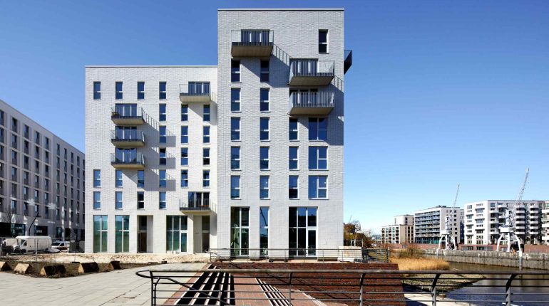 Frontaufnahme des Sportlerhaus in HafenCity Hamburg. An der Straßenecke bildet der hohe Baukörper eine Begrenzung zum Gretchen-Wohlwill-Platz.